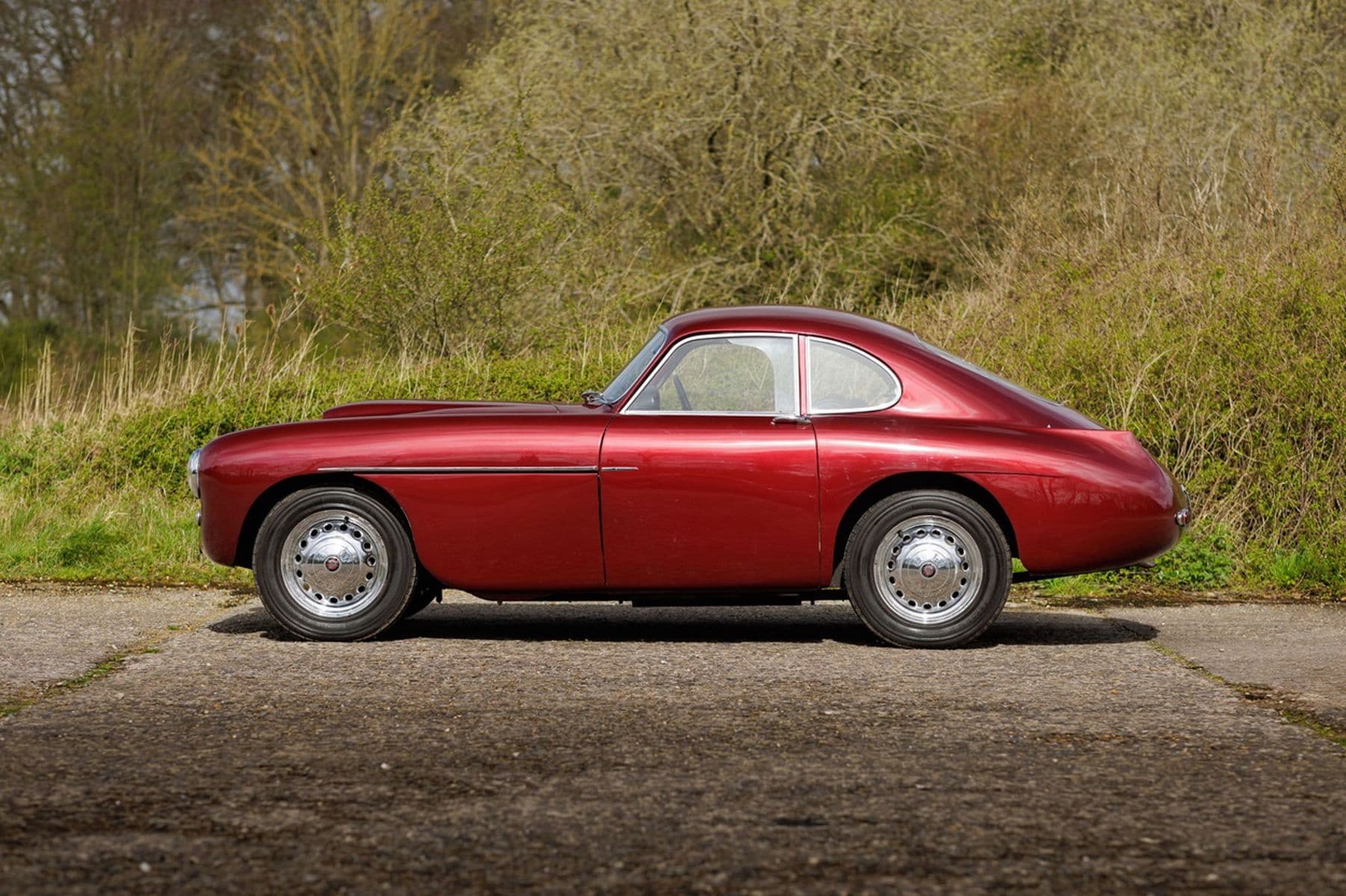 A Bristol 404 in profile, deep red, photographed against an English hedgerow
